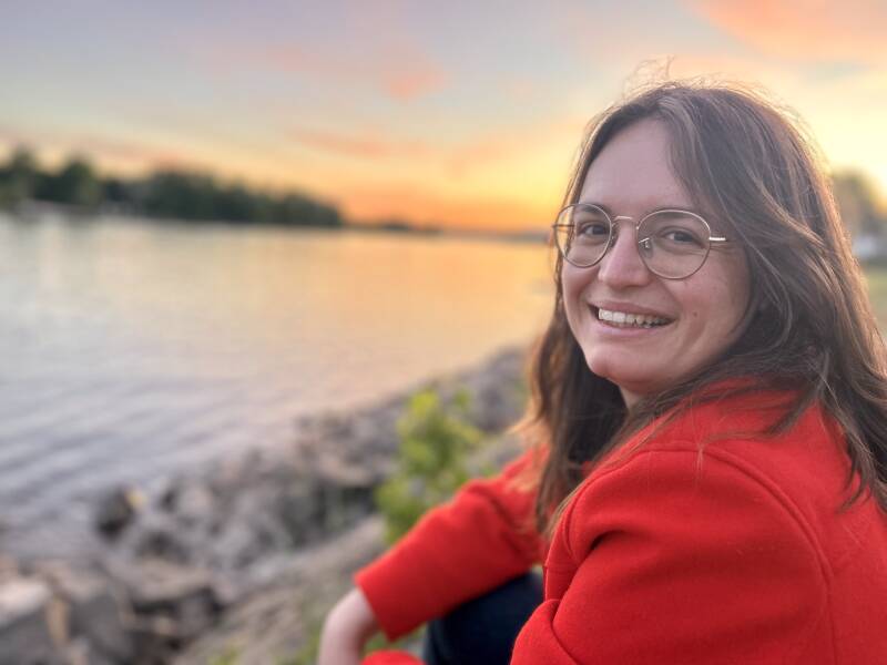Photo of Lara Ammel, UX Designer, smiling at the camera at sundown next to rhine River.