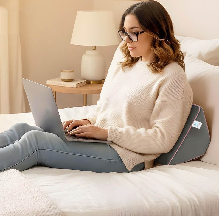 Eine Frau nutzt das Kissen als Rückenstütze und arbeitet am Laptop