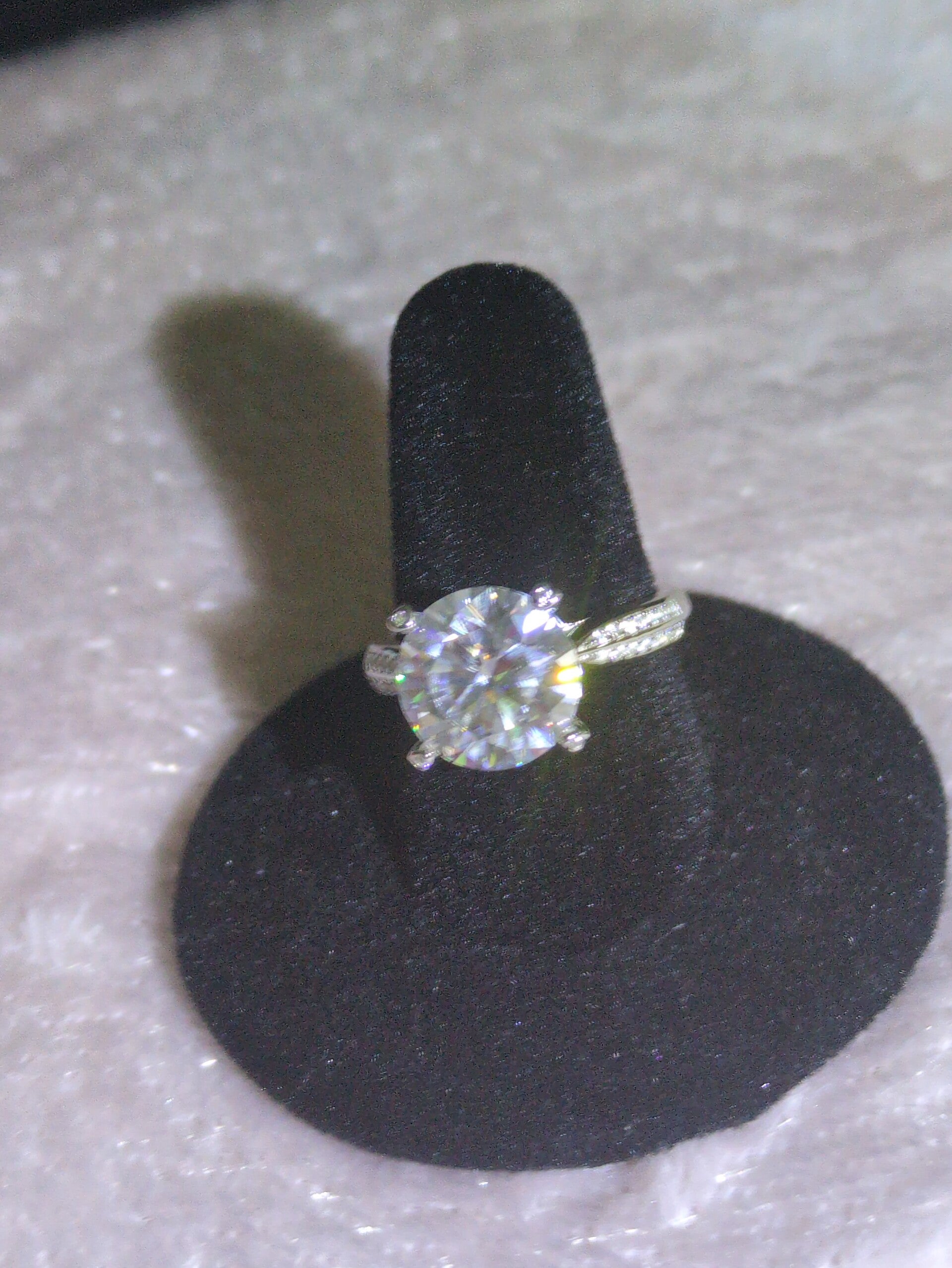 Sz 6 1/2 round-cut engagement ring, featuring a Moissanite center stone set in a six-prong mount with decorative side moissanite accents.