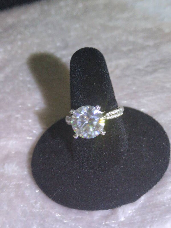 Sz 6 1/2 round-cut engagement ring, featuring a Moissanite center stone set in a six-prong mount with decorative side moissanite accents.