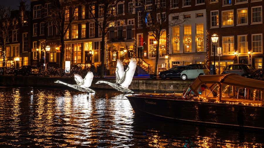 Our wooden boat Venice gliding past the illuminated swans of the Amsterdam Light Festival