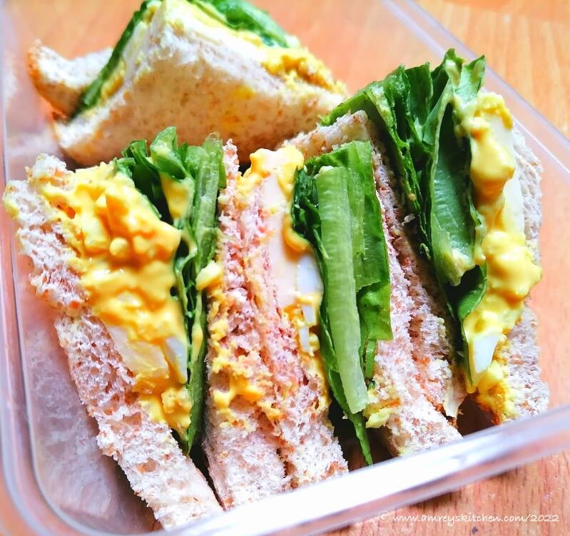 Simud's Egg Sandwich with romaine lettuce in a container on a wooden table. Recipe and photo by Amrey Boquiren of Amrey’s Kitchen™.