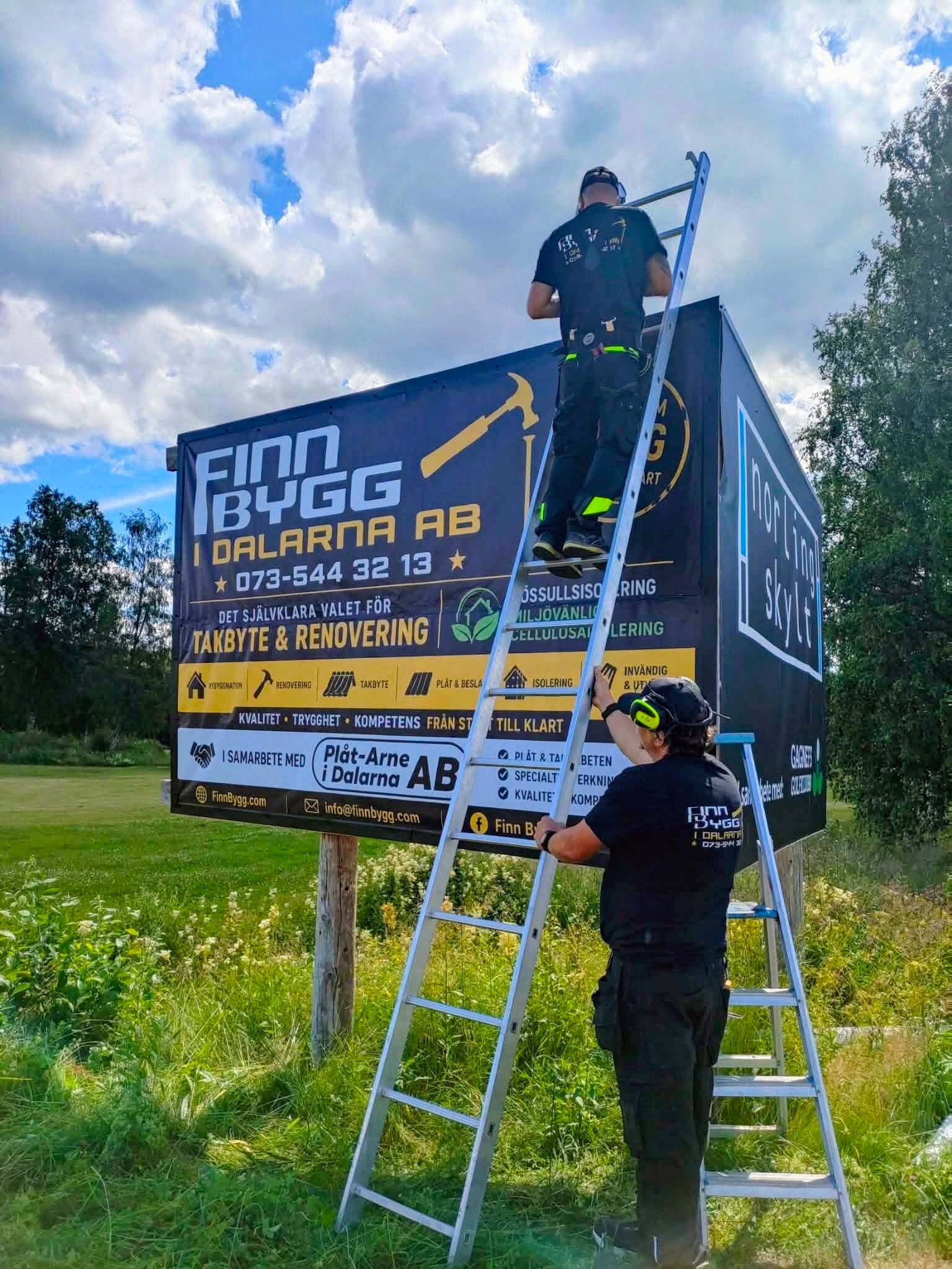 Olof och Magnus från Finn Bygg arbetar vid företagets skylt i Gagnef