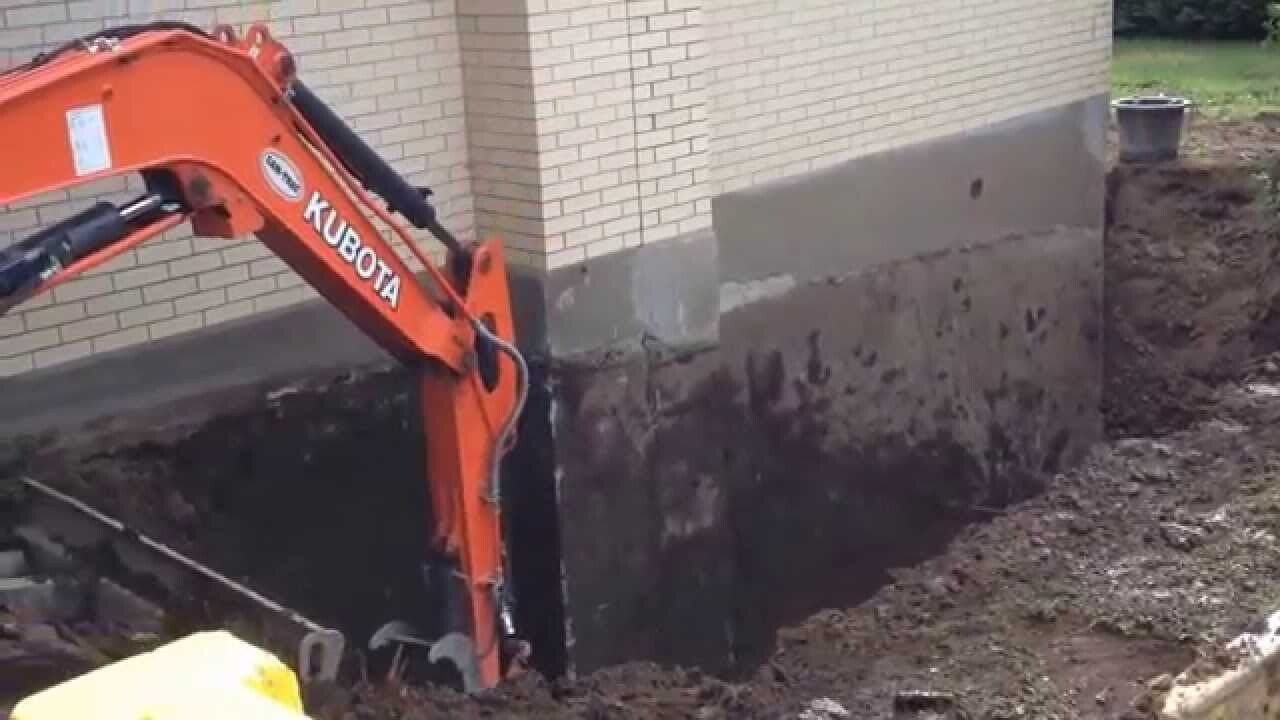 Excavator digging around a house foundation for repair work