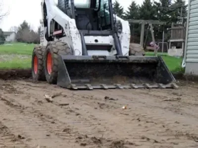 Skid steer grading soil away from a house foundation to improve drainage