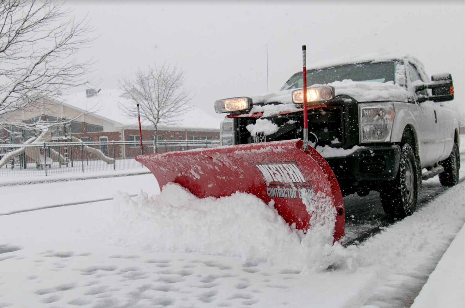 Large snow plow truck removing accumulated snow from a home driveway during winter.