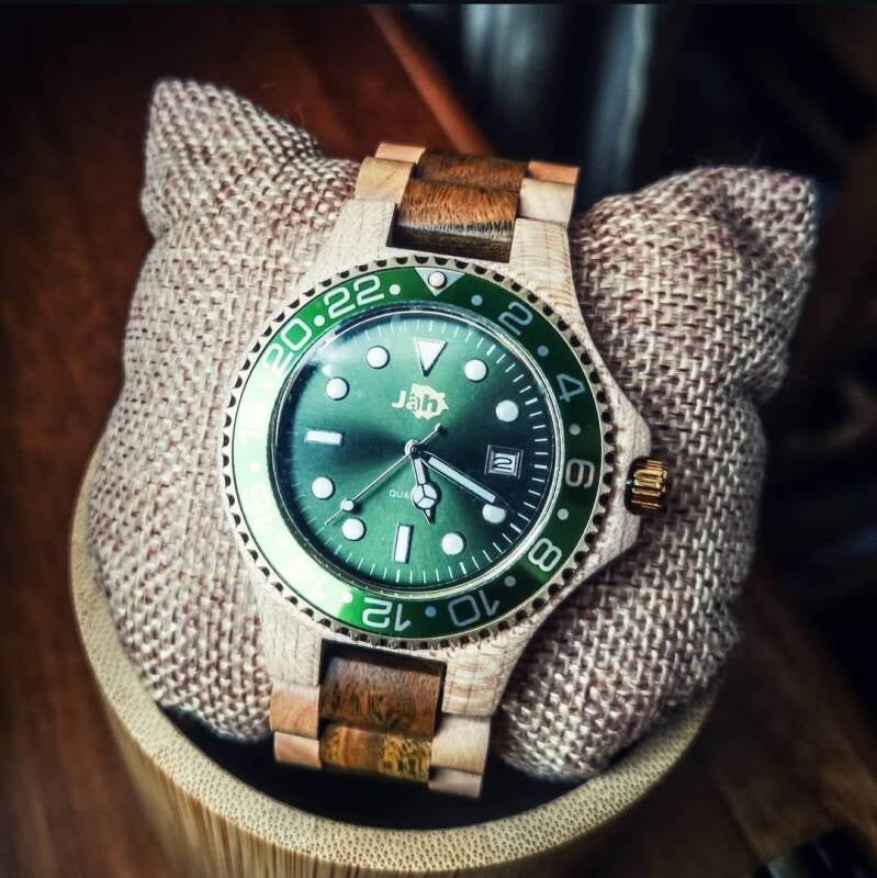 Orologio JAH con quadrante verde scuro e cinturino misto in legno e metallo, posizionato su un cuscino rustico.