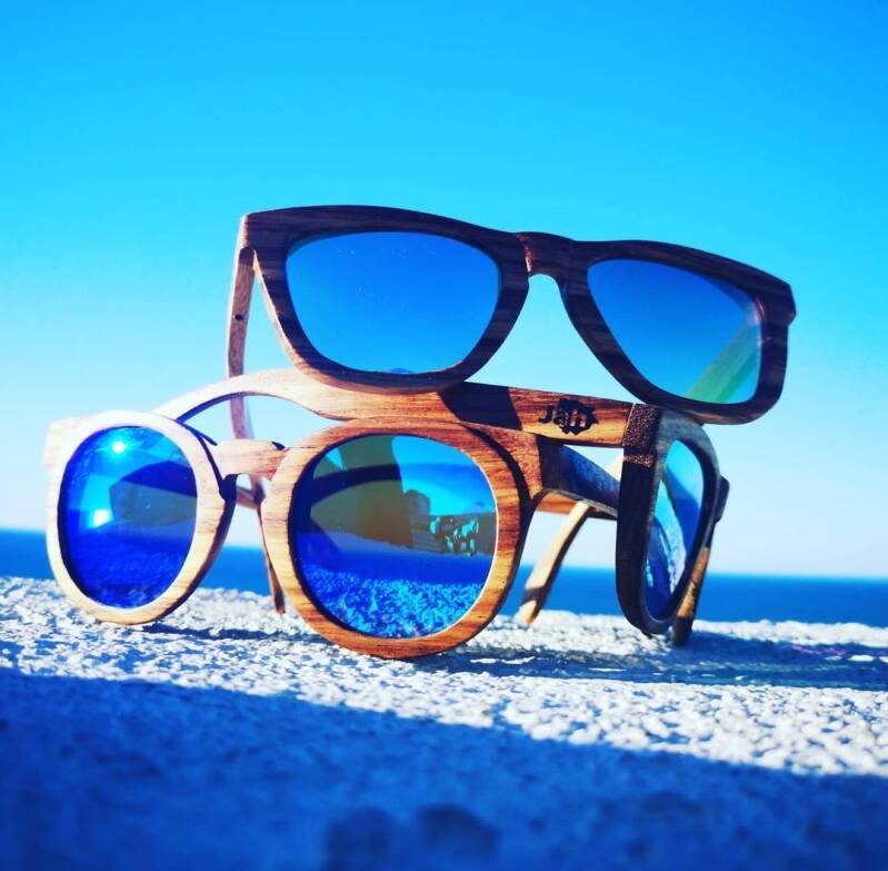 Occhiali da sole artigianali in legno con lenti a specchio blu, unendo stile naturale e protezione UV in un ambiente estivo mozzafiato.