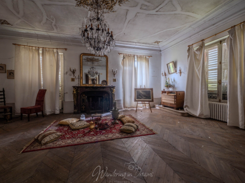 Verlaten chateau in Frankrijk met elegante salon, kroonluchter, vintage haard en gordijnen – urbexinterieur gefotografeerd door Wandering in Dreams.