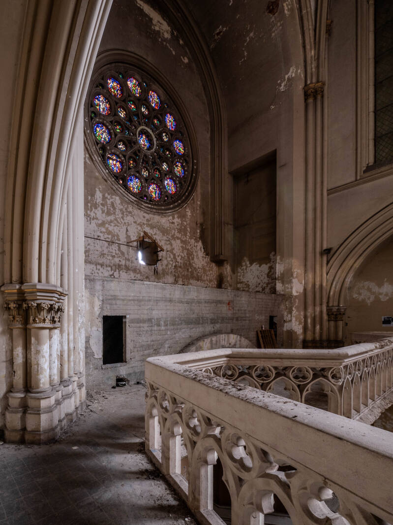 Interieur van een verlaten kerk met groot rond glas in lood raam, verweerde muren en stoffige balustrade vastgelegd tijdens religieuze urbex fotografie in Europa