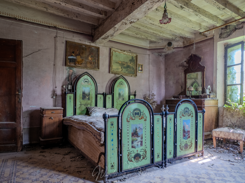 Gedetailleerde urbex-fotografie van het unieke, mintgroene beschilderde metalen bed in de vervallen slaapkamer van de Italiaanse locatie 'Il letto verde dimenticato'. Verweerde muren met oude schilderijen en een balkenplafond omringen het stoffige meubila