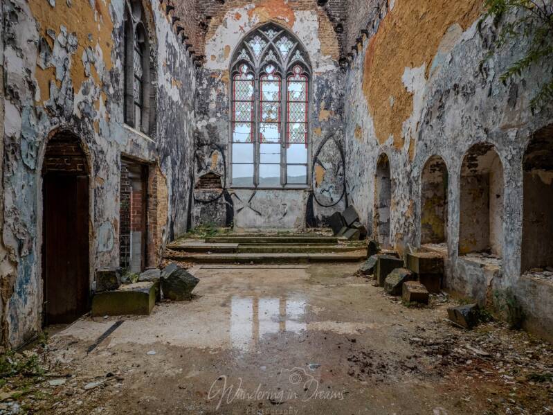 Verlaten kerk met afbladderende verf, gotische ramen en overwoekerde vloer tijdens urbex fotografie van een religieuze locatie in verval