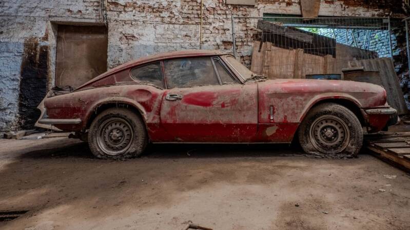 Verlaten rode Triumph sportwagen in Garage Triumph in België bedekt met stof en verval, geparkeerd in een oude industriële garage tijdens urban exploration fotografie door Wandering in Dreams