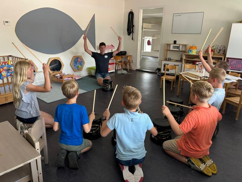 Voorstelling-in-één-dag. Op de foto staat een van de docenten die een workshop percussie geeft aan een groep kinderen.