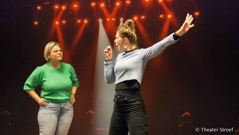 Theaterworkshop volwassenen. Op deze foto staan twee vrouwen. De ene zingt en de andere kijkt toe.