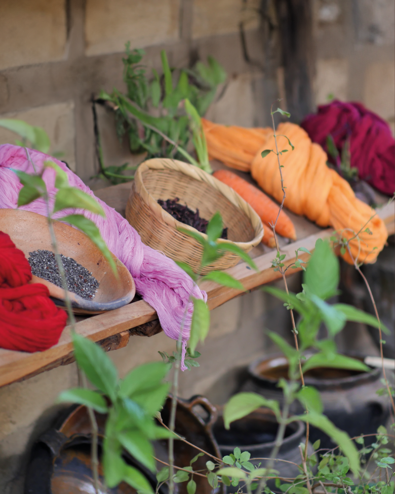Natural dye and textile materials in Guatemala, with orange, red and pink yarns, woven baskets, clay vessels and plants, showing harvest colours, craft and artisanal colour inspiration.