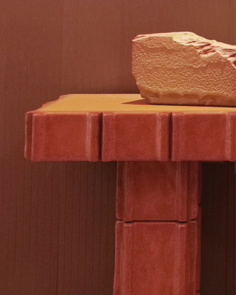Terracotta red ceramic table with a soft orange surface and rough textured stone object, showing warm earthy orange tones, glaze, texture and material contrast in interior design.