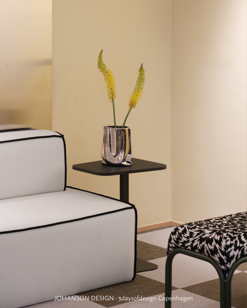 Soft interior setting by Johanson Design with a black side table, black chair pattern and graphic black lines against pale upholstery.