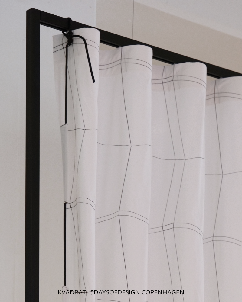 White Kvadrat curtain with fine black contour lines, showing black as a graphic textile detail in a soft interior palette.