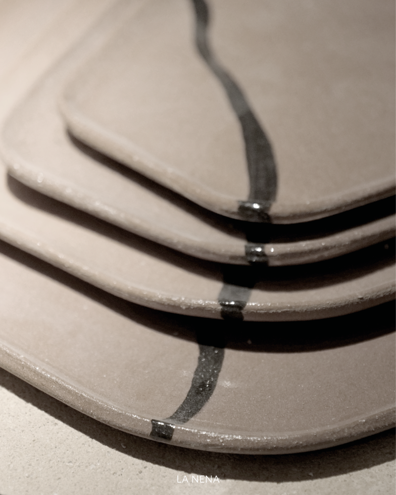 Close-up of ceramic plates with black painted lines, showing black as a fluid graphic mark on a soft neutral surface.