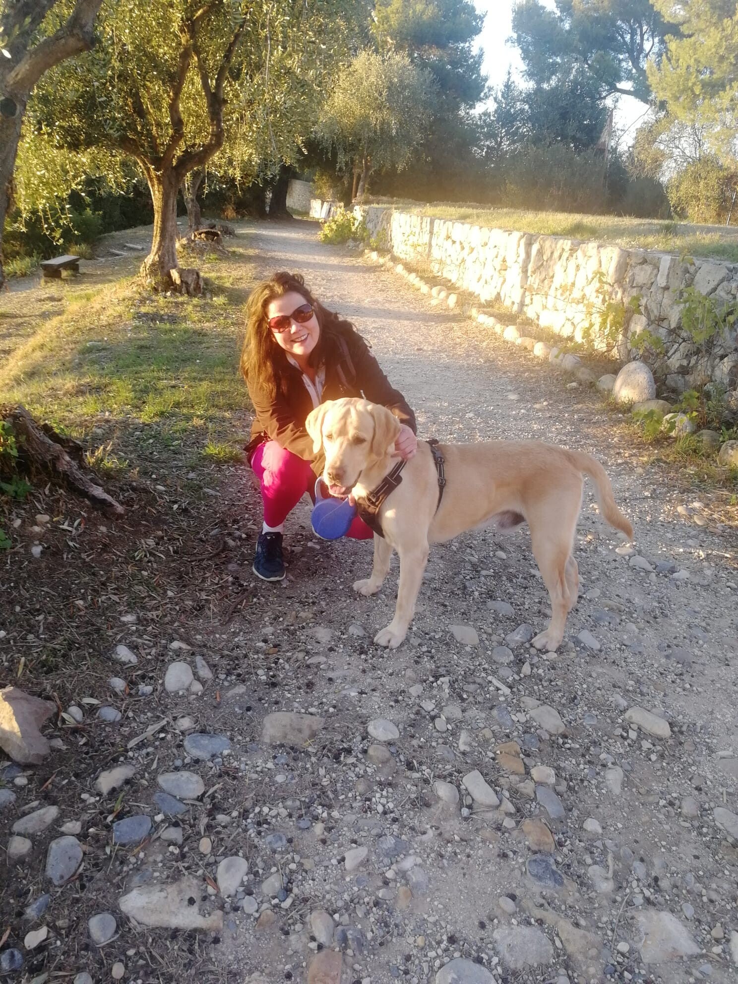 Amanda kneeling with a yellow Labrador named Gino on a country path in Nice, France.