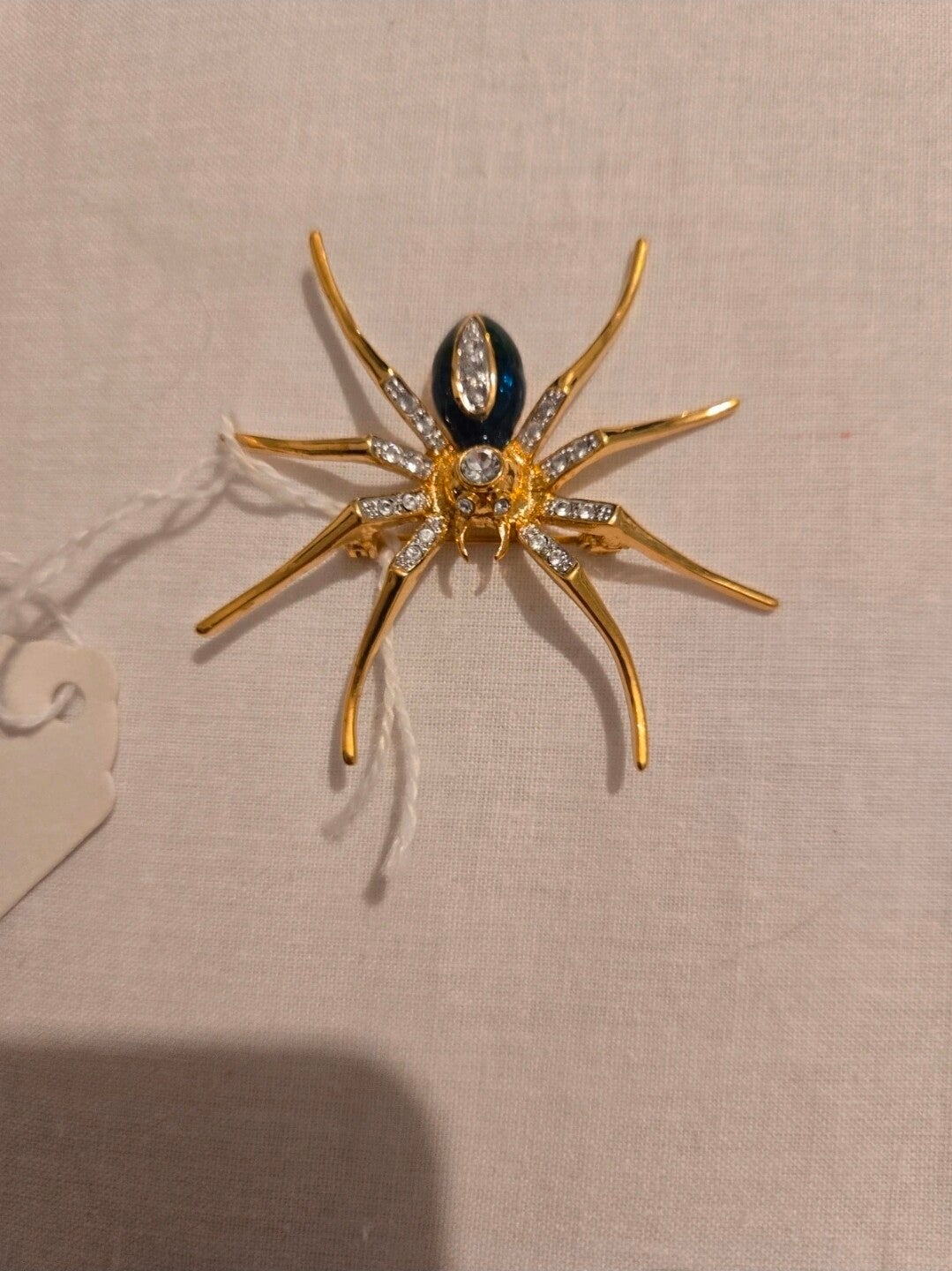 This gold-tone spider brooch features a hinged pin fastening and an textured metal finish.