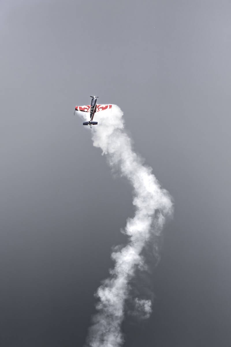 Photographie d’un avion Extra 330 EVAAE de l'Équipe de Voltige de l’Armée de l’Air et de l’Espace, en montée verticale avec traînée de fumée blanche, ciel clair en toile de fond.