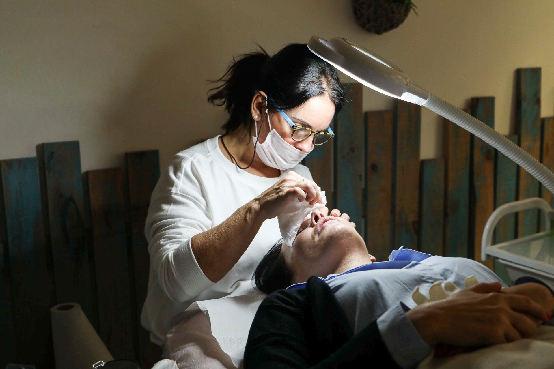 Profesional sanitaria con mascarilla y guantes realizando un tratamiento en el contorno de ojos