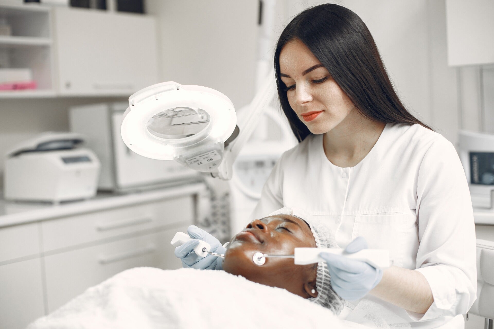 Profesional sanitaria con guantes valorando la piel del rostro de una paciente bajo una lámpara