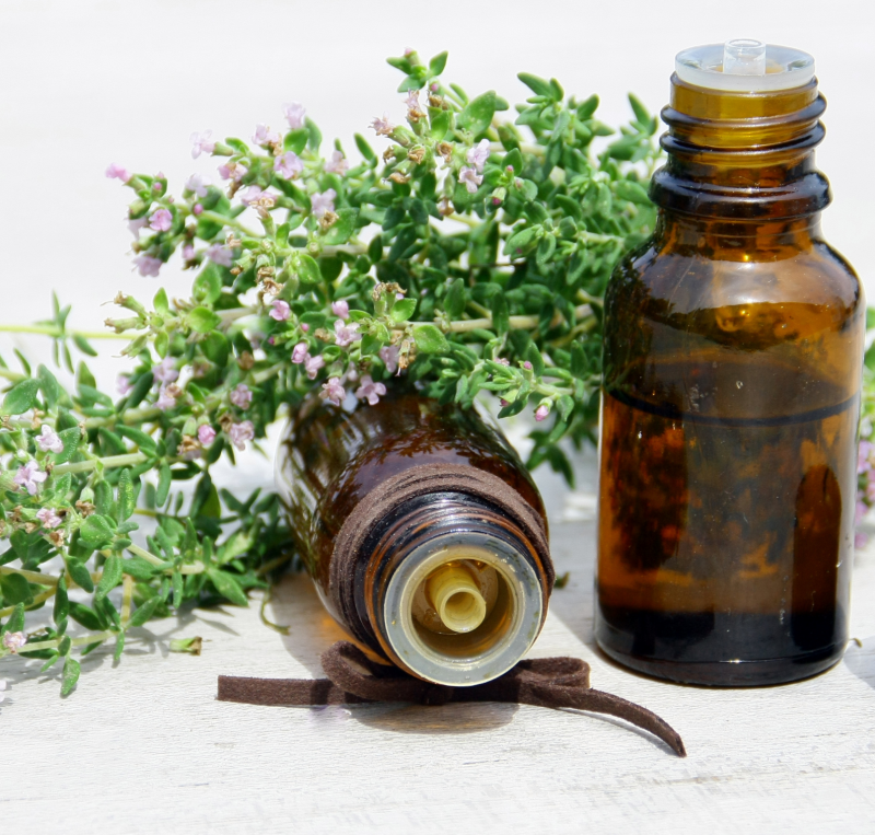 Huile essentielle de thym avec brins frais – flacon ambré sur fond vert.