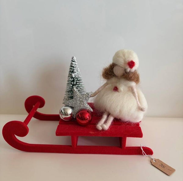 Filzfee in weiß auf ihrem roten Weihnachtsschlitten