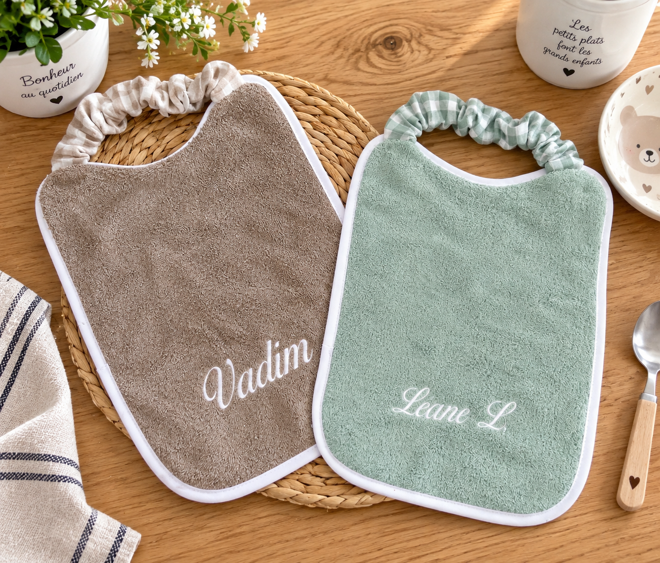 Deux bavoirs de cantine à col élastiqué, taupe et vert d'eau, personnalisés avec les prénoms Valentin et Léane brodés