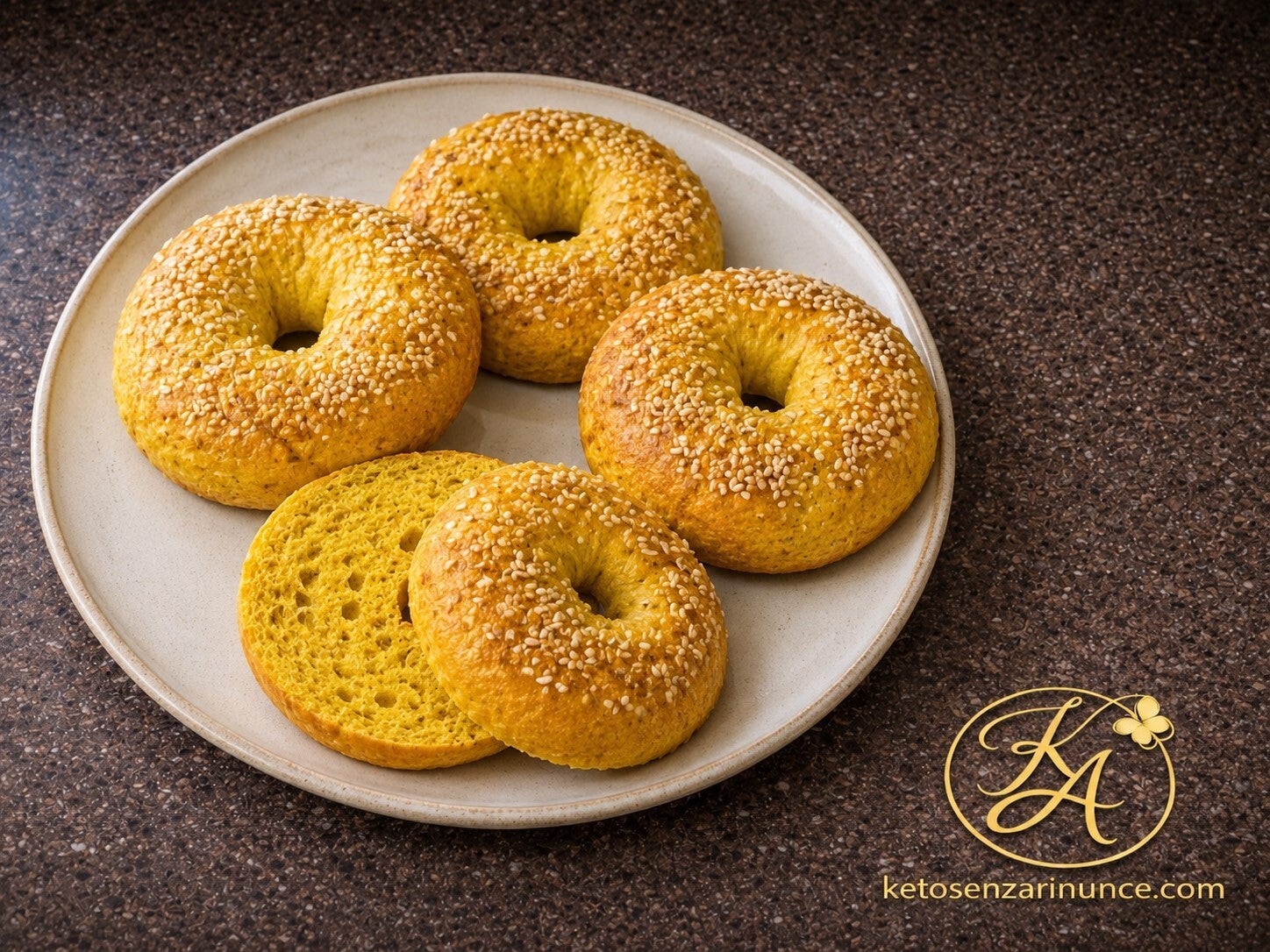 Bagel chetogenici salati alla curcuma, dorati e soffici, decorati con semi di sesamo e serviti su un piatto chiaro. Una ricetta keto gustosa e senza rinunce, ideale per colazioni salate, brunch o accompagnamenti sfiziosi.