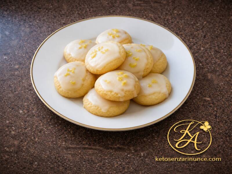 Biscottini da tè al limone glassati chetogenici, morbidi e profumati, serviti su piatto bianco con bordo dorato sullo sfondo marrone del blog Keto senza rinunce.