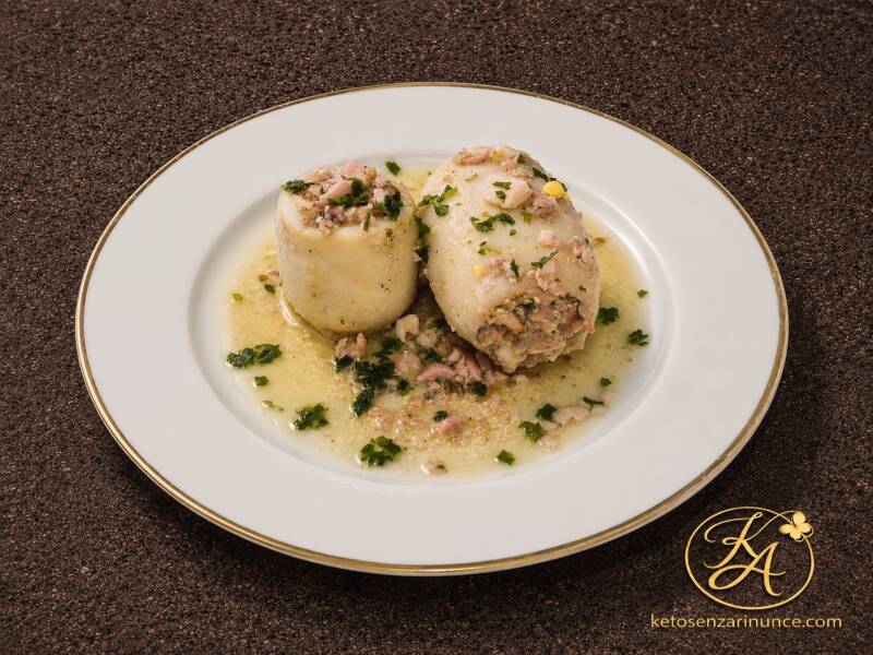 Calamari ripieni keto con uova sode e acciughe, serviti su piatto bianco elegante con bordo dorato, con prezzemolo fresco e sughetto leggero, su sfondo marrone speckled con logo KA e riferimento a ketosenzarinunce.com. Immagine raffinata per il blog Keto 