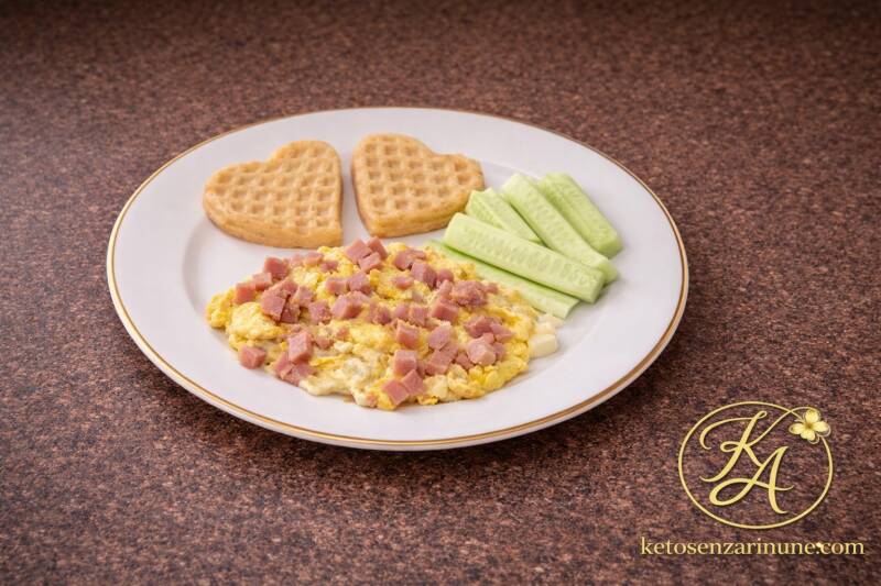 piatto con uova strapazzate e prosciutto, waffle a cuore e cetriolo chetogenico, colazione salata semplice e completa
