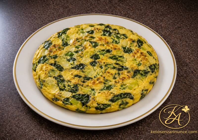 Frittata chetogenica con spinaci e porri, morbida, saporita e leggermente dorata, servita su un elegante piatto bianco con bordo dorato.