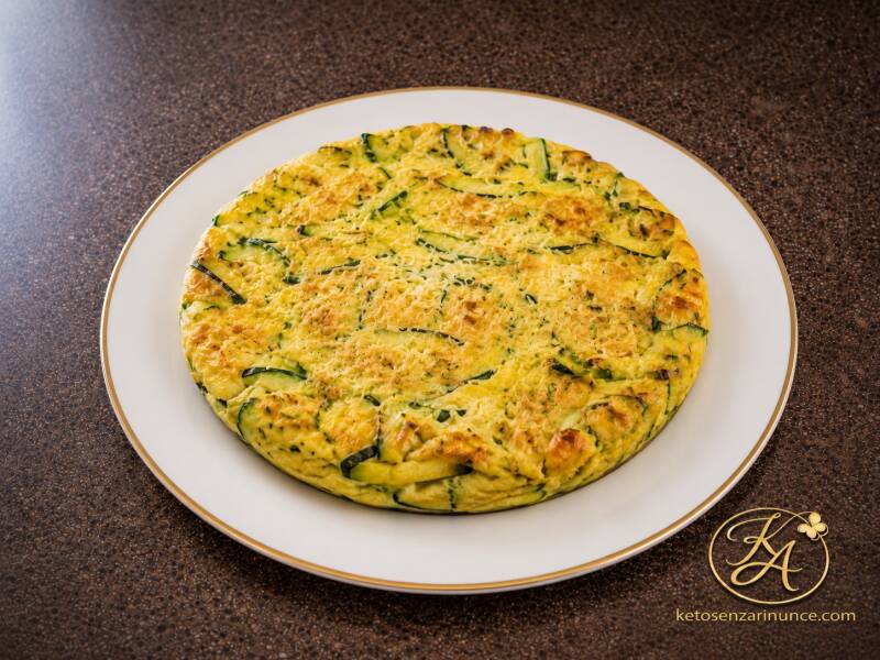 Frittata chetogenica di zucchine con parmigiano, morbida all’interno e leggermente dorata, servita su un elegante piatto bianco con bordo dorato.