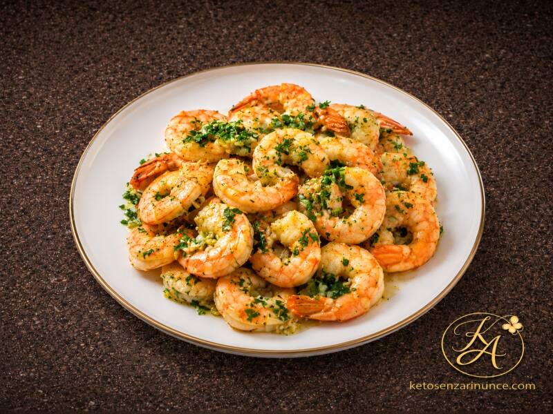 Gamberoni cotti con prezzemolo, serviti su un elegante piatto bianco con bordo dorato. Immagine raffinata e appetitosa, ideale per una ricetta semplice e gustosa.