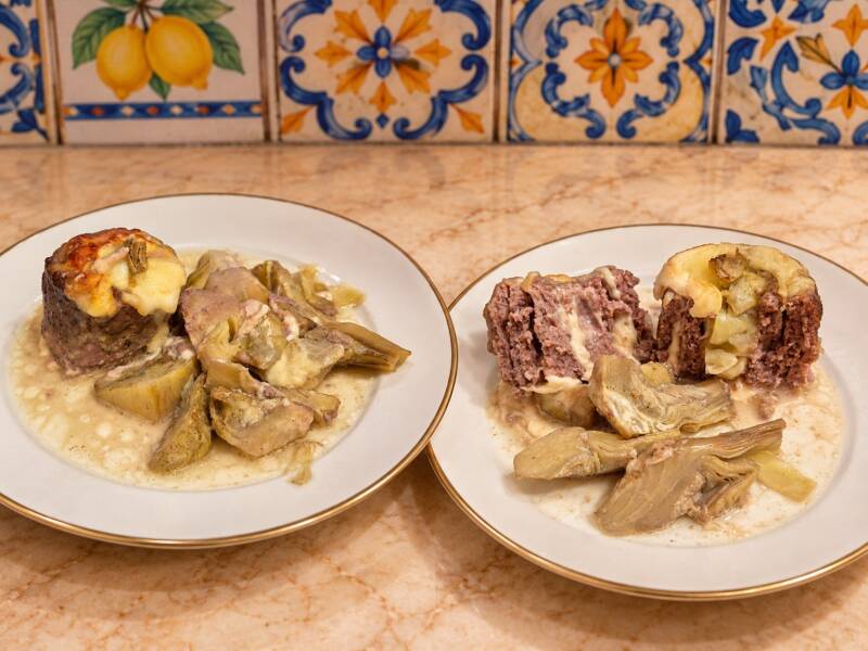 Due porzioni di girelle di carne macinata con formaggio e carciofi, servite con il fondo cremoso di cottura; una girella intera e una aperta per mostrare il ripieno.