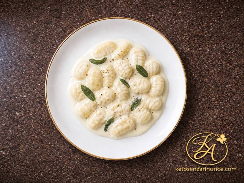 Gnocchi chetogenici alla ricotta con crema al formaggio e salvia, serviti in un piatto bianco con bordo oro su sfondo marrone speckled del blog Keto senza rinunce.