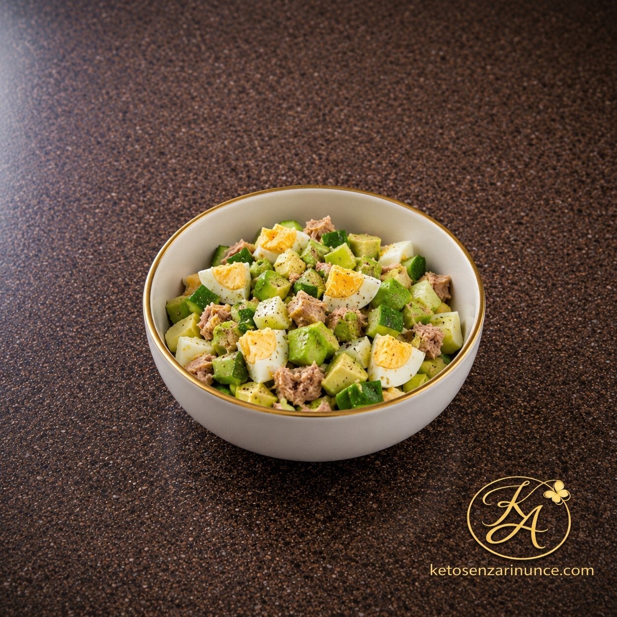 Insalata chetogenica con uova sode, tonno, avocado e cetriolo, servita in una ciotola bianca con bordo dorato su sfondo marrone elegante.