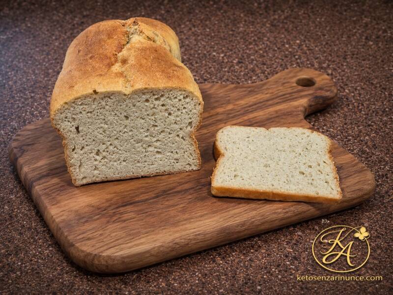 Pan brioche chetogenico morbido fotografato su tagliere in legno con una fetta tagliata accanto. Immagine in stile blog con sfondo marrone e logo Keto Amica, ideale per presentare una ricetta keto soffice, versatile e adatta a colazione, toast e French to