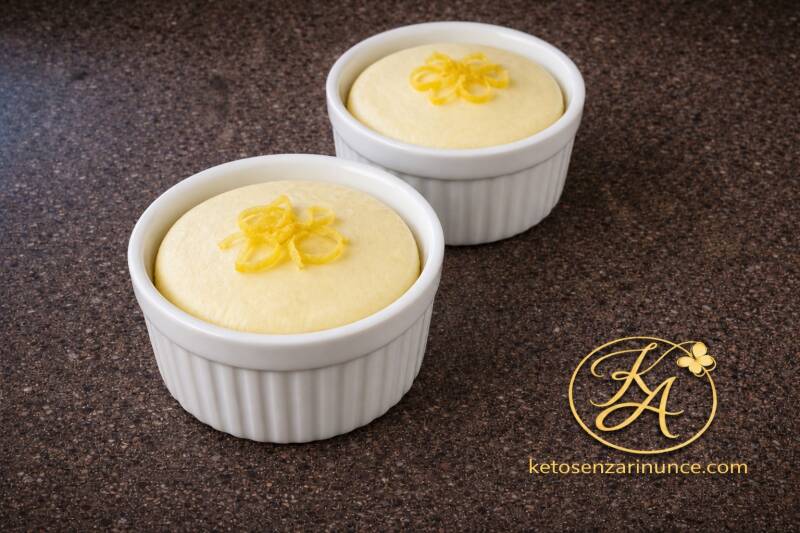 Mini cheesecake chetogenica in tazza servita in due ramekin bianchi su sfondo marrone speckled del blog ketosenzarinunce.com, dolce keto cremoso al limone cotto al microonde.