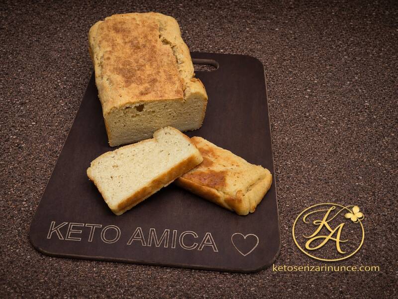Pane chetogenico proteico con mozzarella e panna, tagliato a fette e servito su tagliere scuro Keto Amica, su sfondo marrone speckled con logo KA e riferimento a ketosenzarinunce.com. Ricetta keto salata compatta, saziante e perfetta da tostare, per il bl