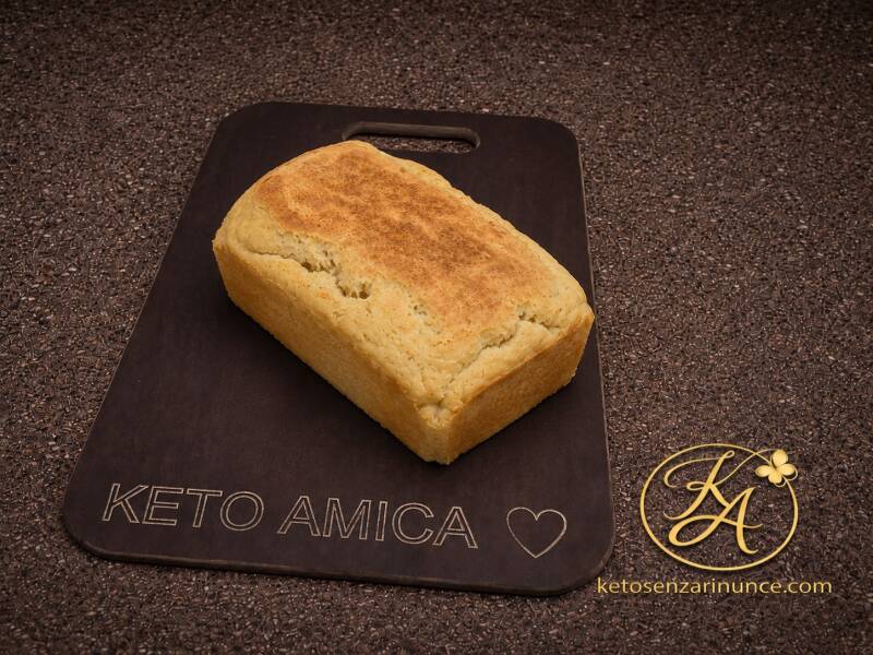 Pane chetogenico proteico con mozzarella e panna, presentato come pagnotta intera su tagliere scuro Keto Amica, su sfondo marrone speckled con logo KA e riferimento a ketosenzarinunce.com. Immagine elegante per il blog Keto senza rinunce, adatta a una ric