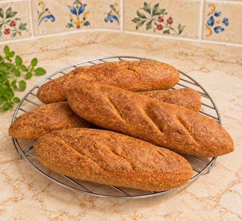 Quattro filoncini di pane keto lievitato, dorati e disposti su una griglia. Ricetta fatta in casa senza uova, latticini e farina di mandorle.