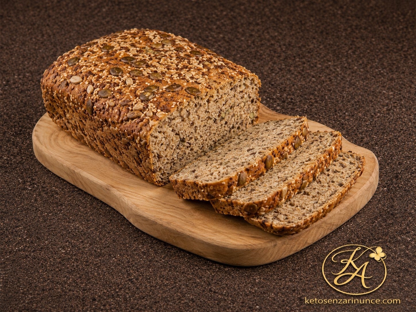 Pane rustico chetogenico ai semi in versione asciutta, presentato su un elegante tagliere in legno con alcune fette tagliate in evidenza. Crosta dorata ricca di semi misti e mollica compatta, ideale da servire a fette, tostare o accompagnare a piatti sala