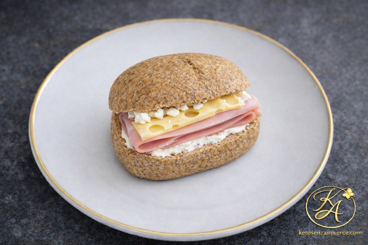 Panino chetogenico morbido e dorato, farcito con prosciutto cotto e formaggio, servito su piatto bianco con bordo dorato.