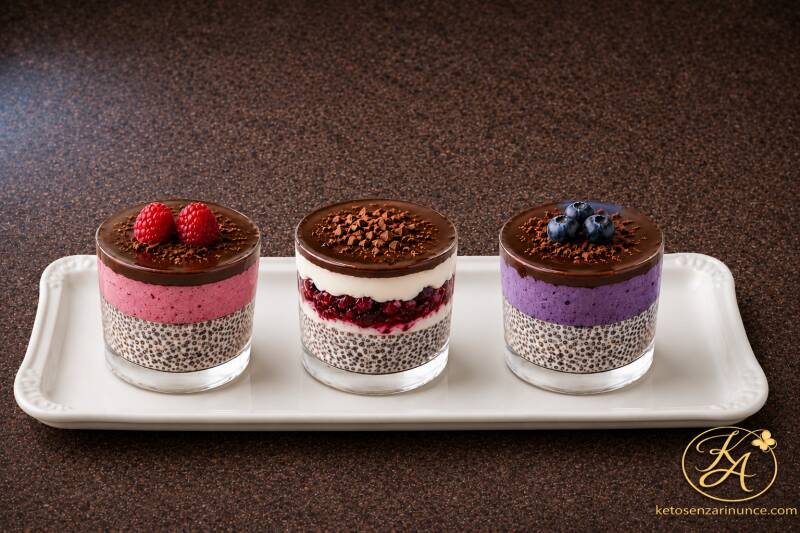 Bicchierini keto con ricotta, chia, mousse ai frutti rossi e cioccolato fondente croccante serviti su vassoio bianco elegante. Dessert low carb e keto friendly di Keto senza rinunce.